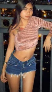 Rose F leans against balcony in loose shorts and revealing top